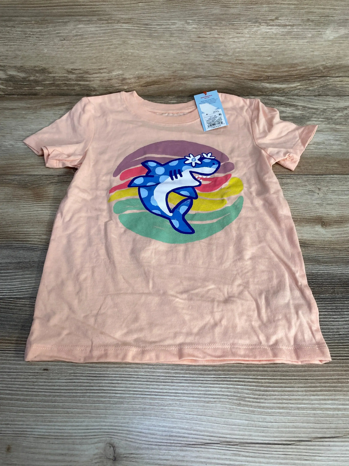 Flat lay of peach Cat & Jack toddler t-shirt size 4T showing large blue shark graphic and attached tag on wood background