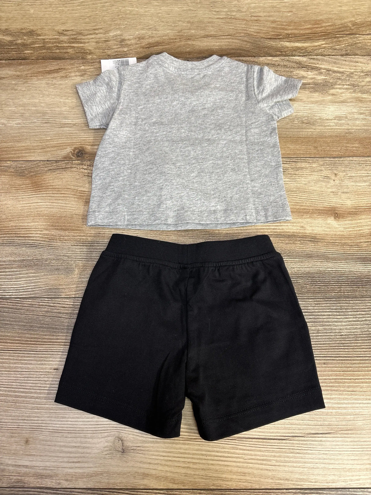 Flat lay Moschino baby tee and shorts showing grey tee (back) and black elastic-waist shorts on wood background