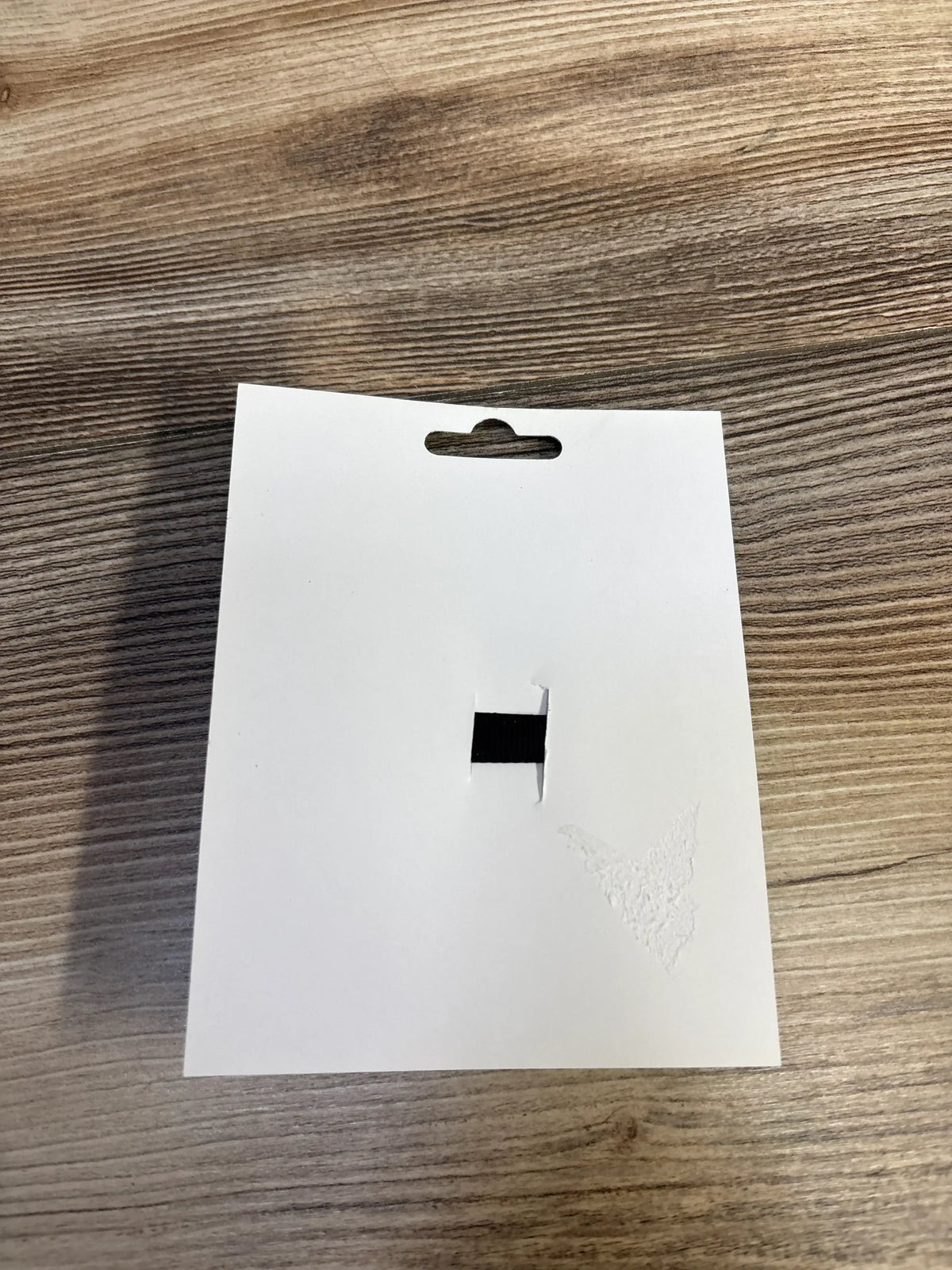 Blank white product tag with hang hole on wood surface, for kids or maternity items