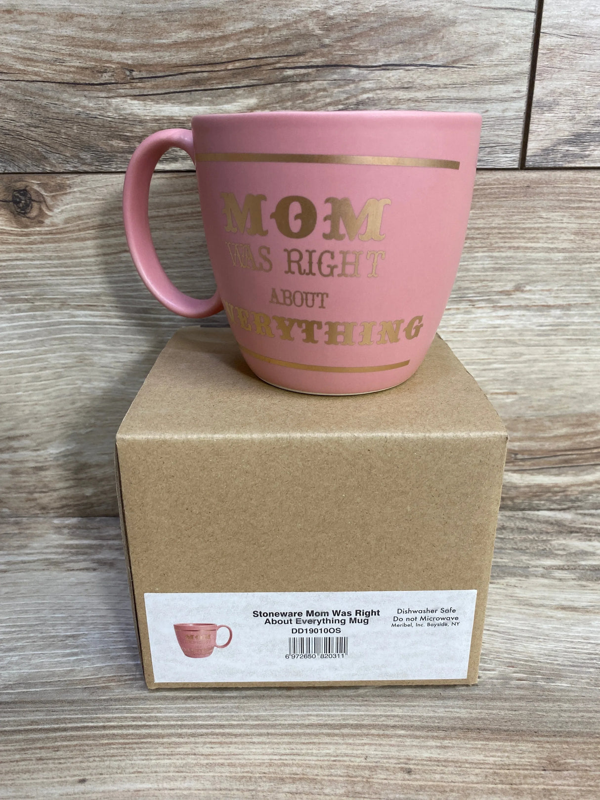 Three-quarter view of NEW pink stoneware Mom Was Right About Everything mug with gold lettering atop original kraft box on wood plank floor