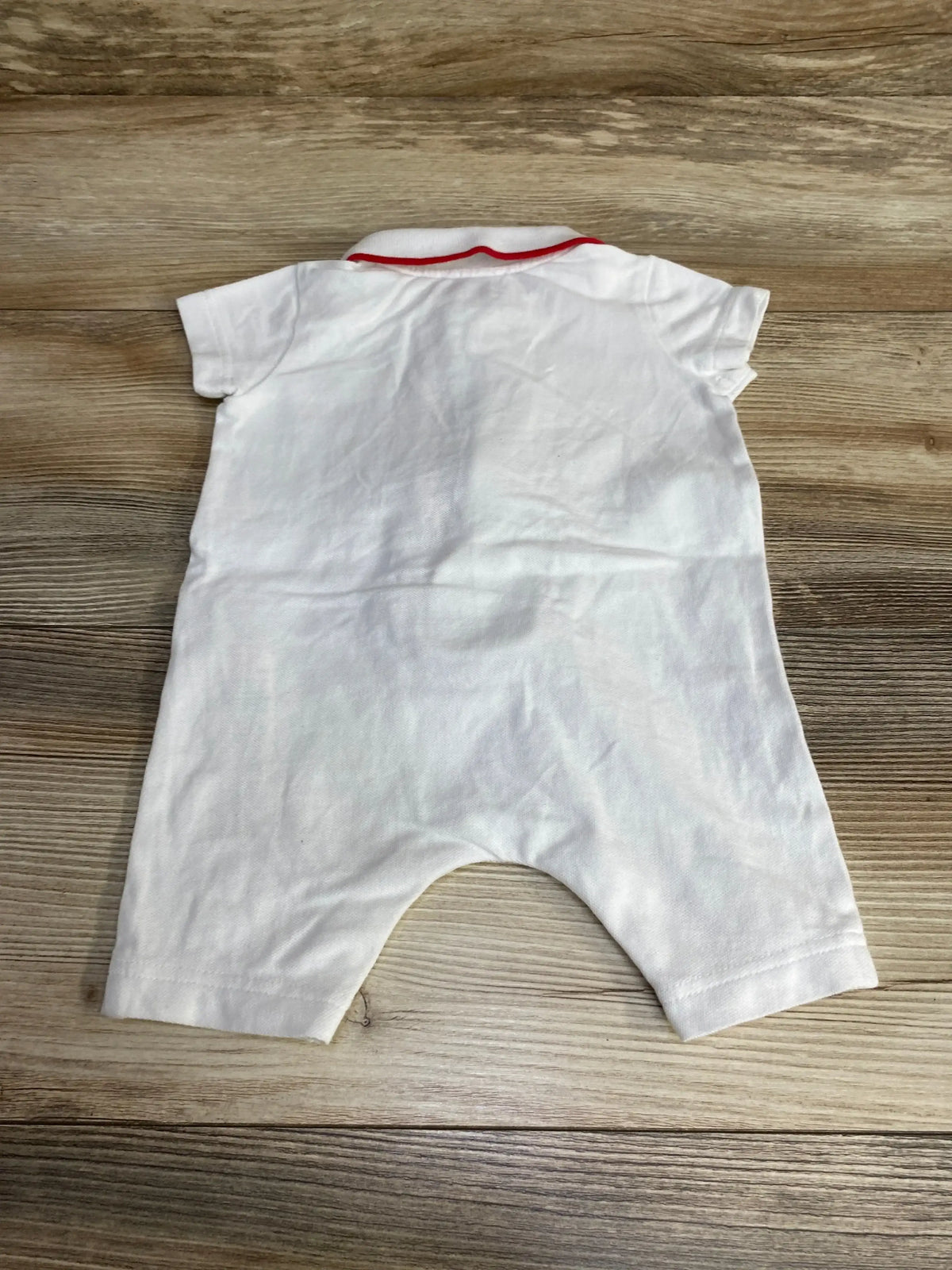Back view of white Burberry polo romper showing red trimmed collar, short sleeves, and short legs on wood background