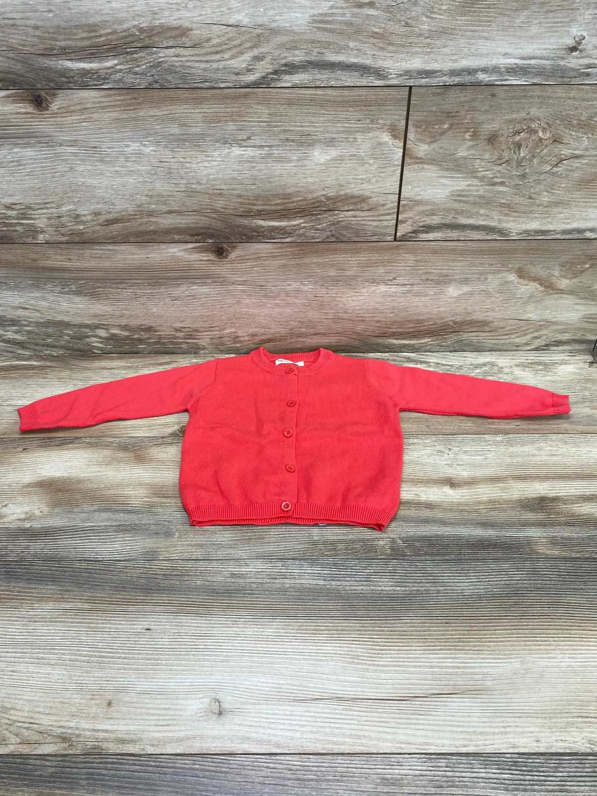 Flat lay of pink baby cardigan size 12 months showing front buttons and crew neck on wooden background