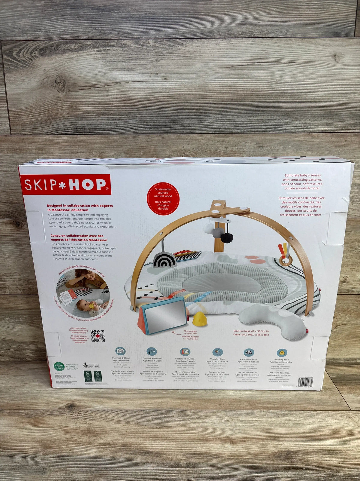 Back of NEW Skip Hop Discoverosity Play Gym box showcasing wooden arch with mat and feature icons on wood plank floor