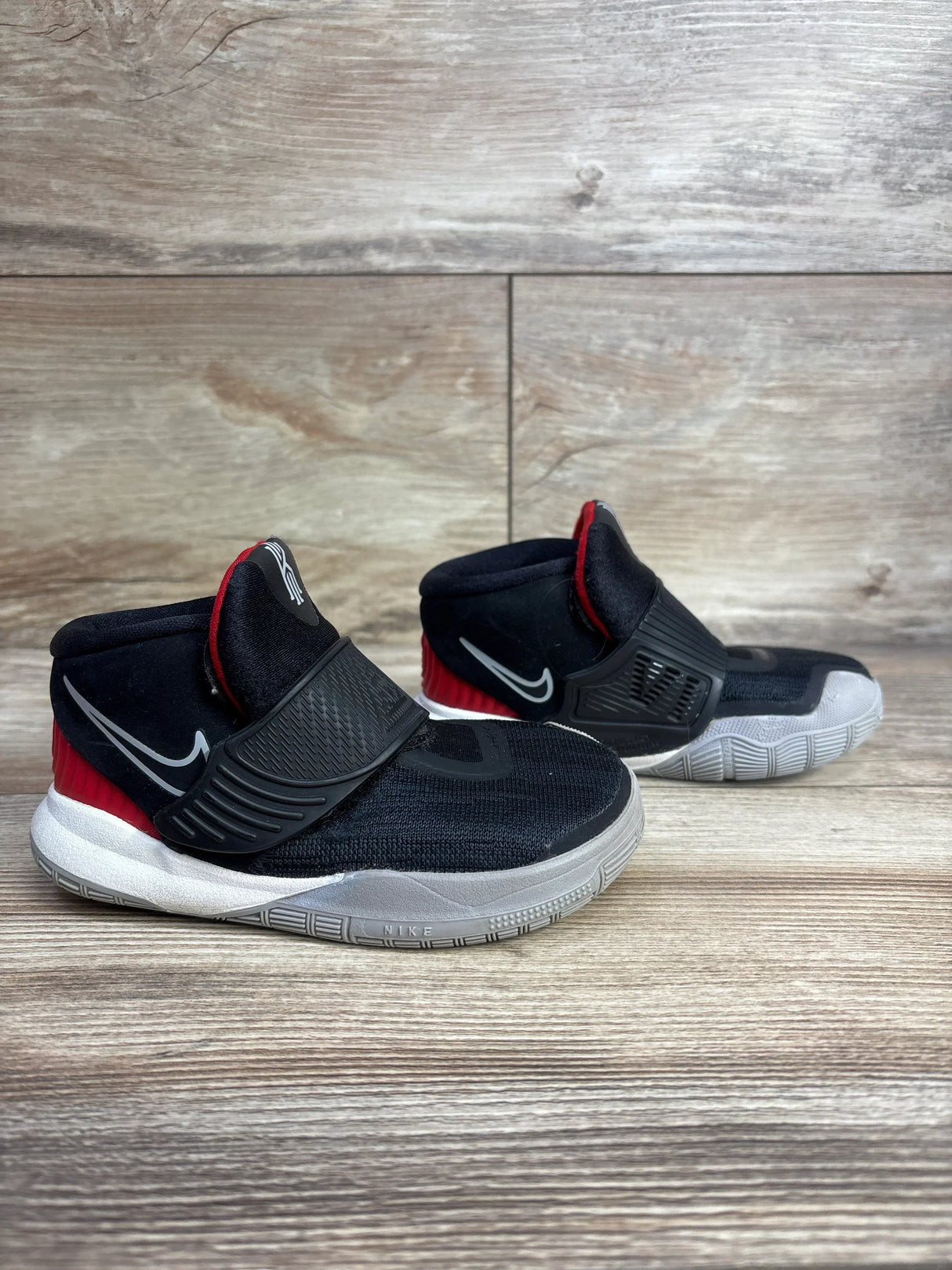 Black and red kids Nike sneakers with Velcro strap and white soles on wood background