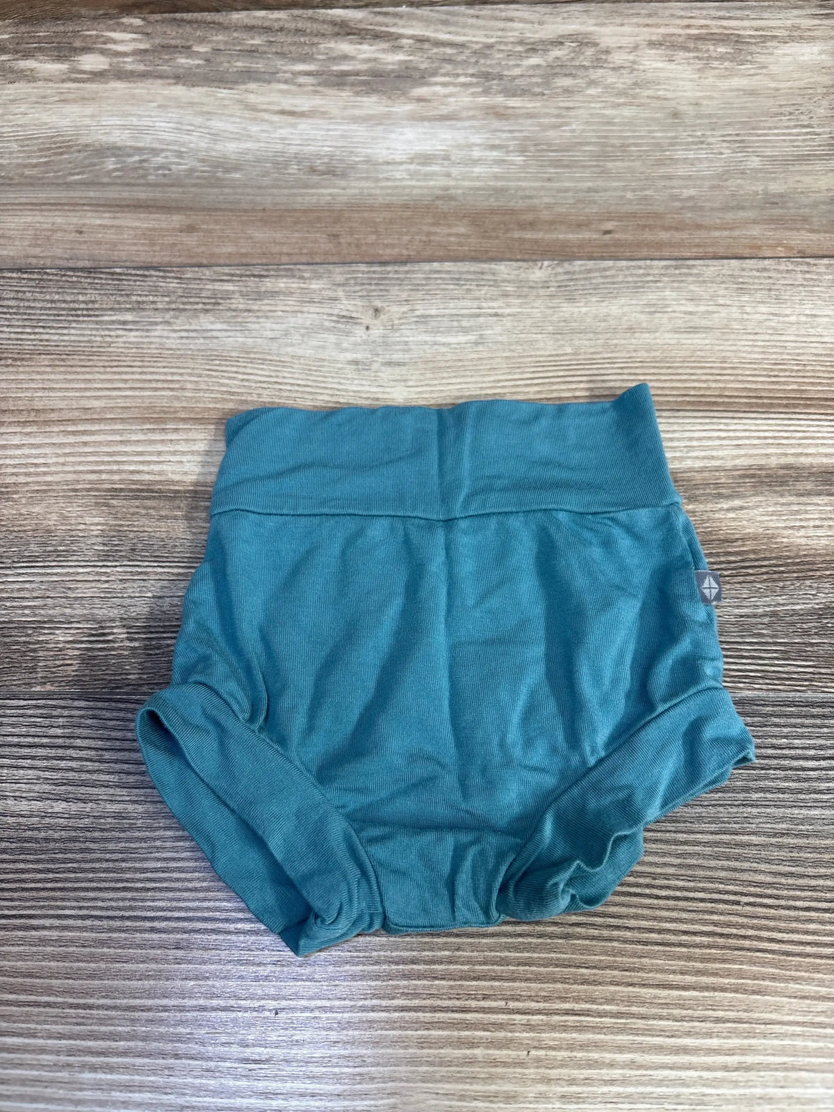 Flat lay of teal Kyte Baby bamboo bummies, newborn 0-3M, showing high fold-over waistband and gathered leg openings on wood background