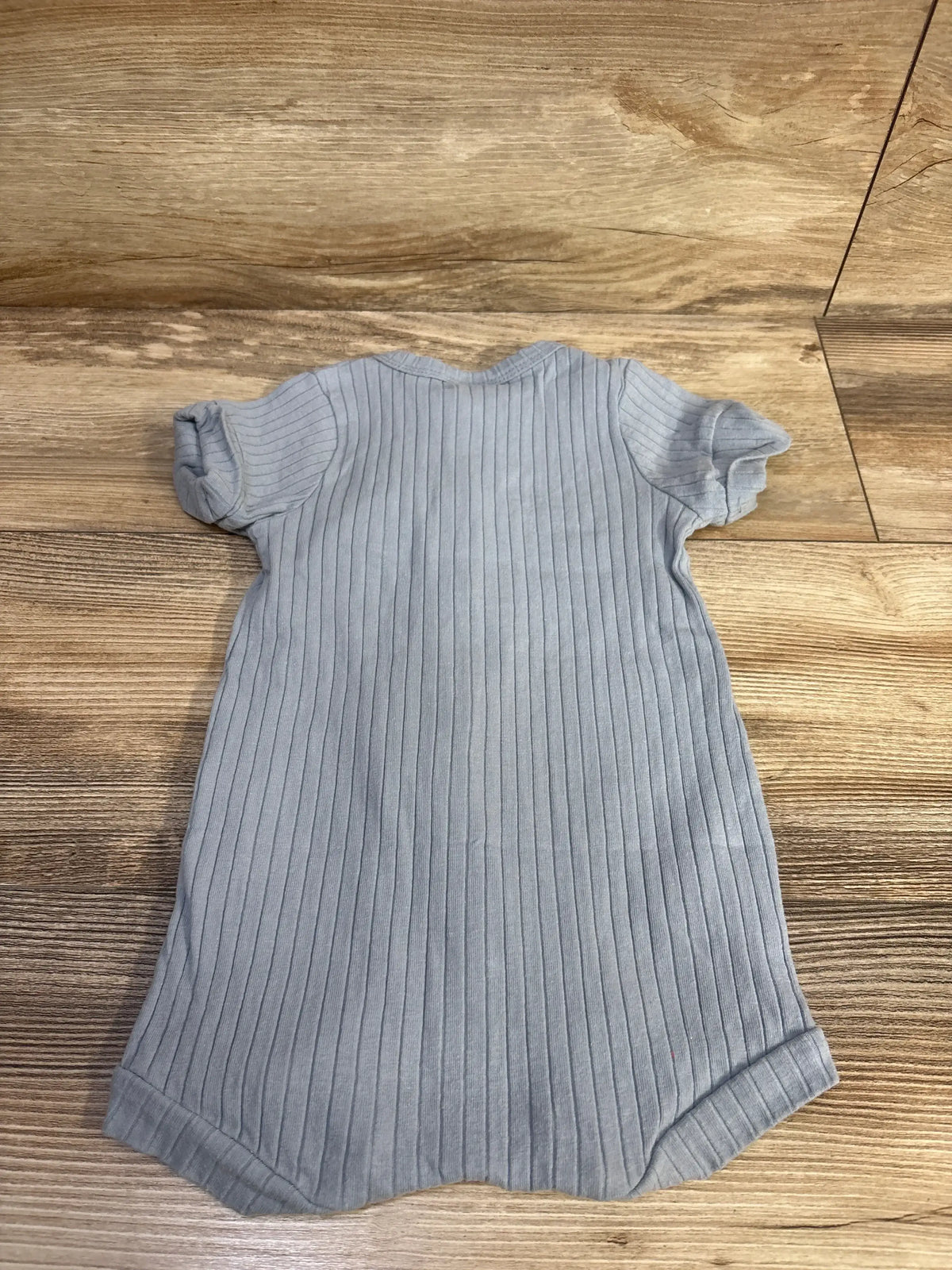 Top-down view of blue ribbed shortie romper showcasing vertical ribbing, short sleeves, and cuffed leg openings on a wood floor