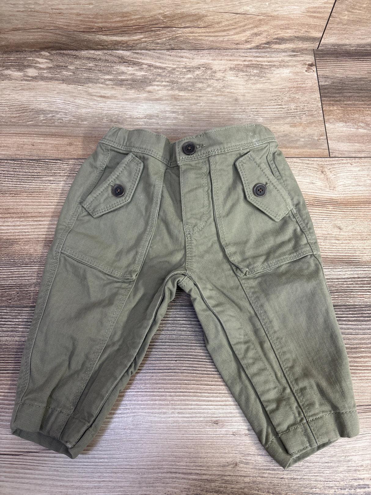 Toddler olive green cargo pants with buttoned flap pockets on wooden floor