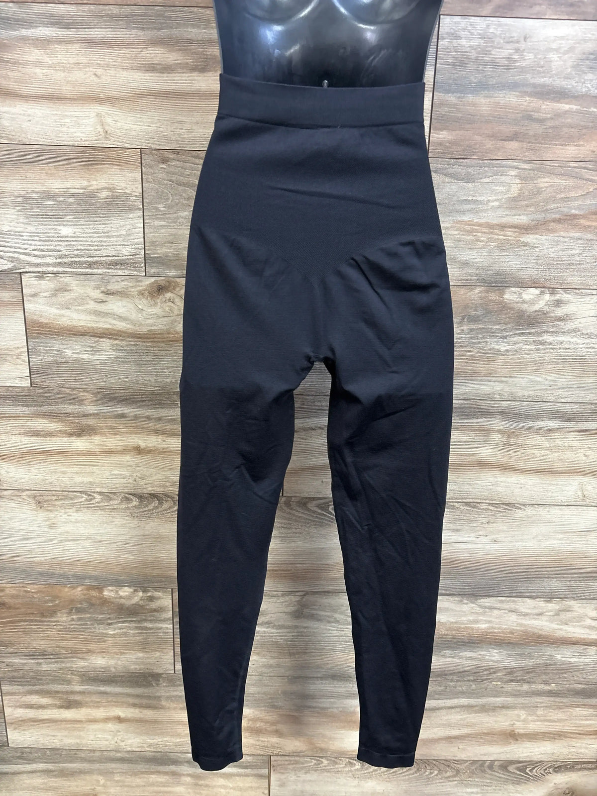 Front view of black belly support maternity leggings showcasing full-length legs and a wide waistband on a wood floor