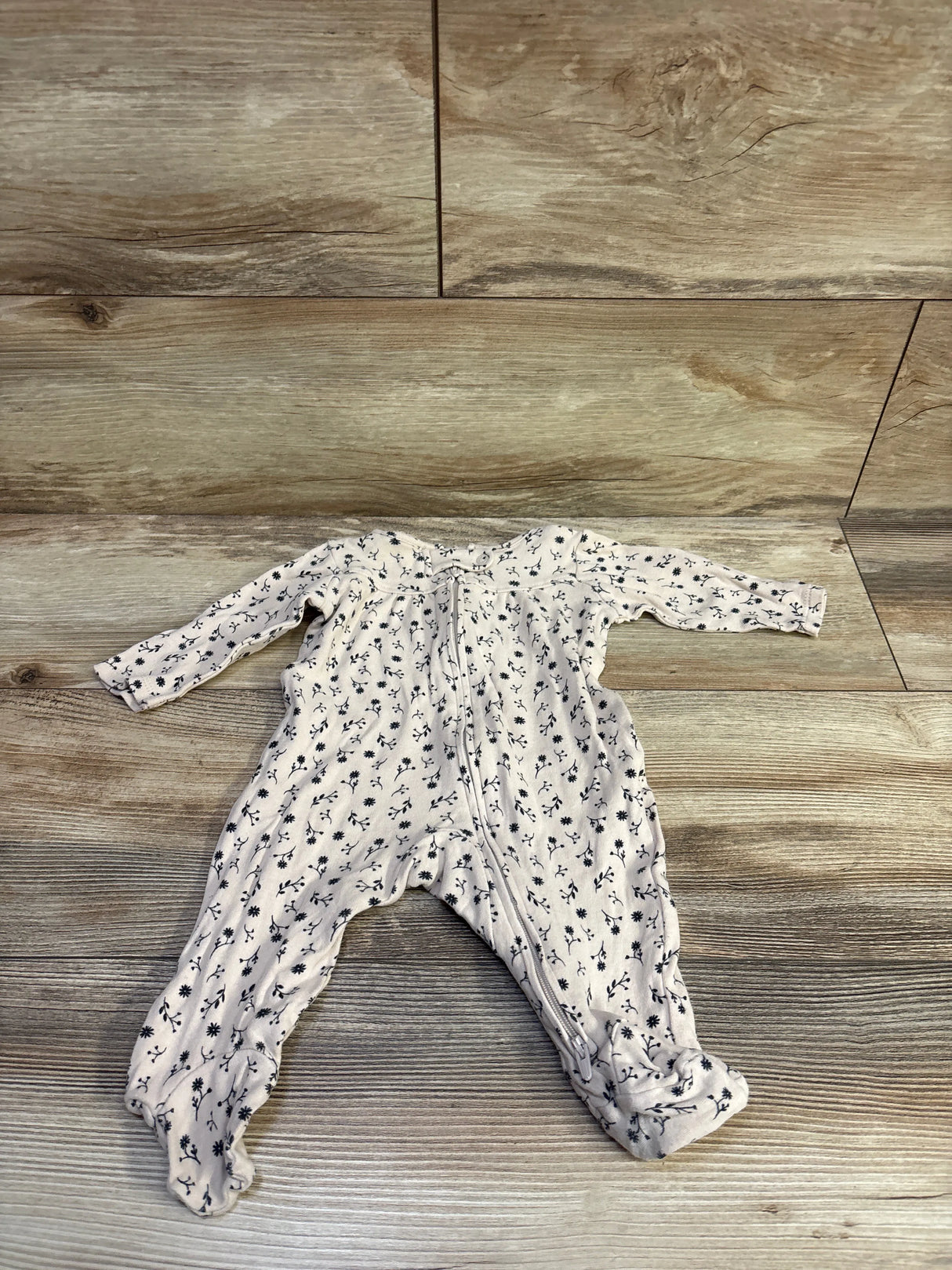 Top-down view of beige floral footed sleeper showing front zipper and all-over navy floral print on a wood floor background