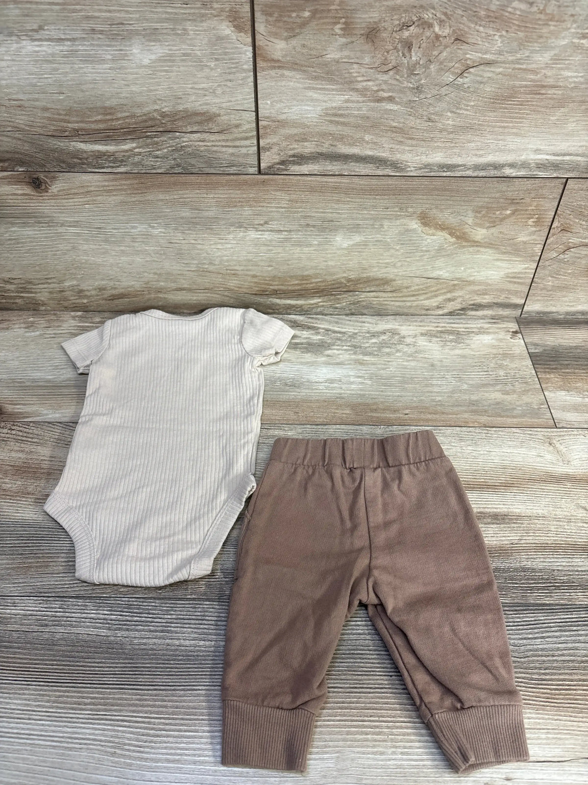 Top-down of Carter's 2-piece ribbed beige bodysuit and brown pants showing ribbed texture, elastic waist and cuffed ankles on wood background