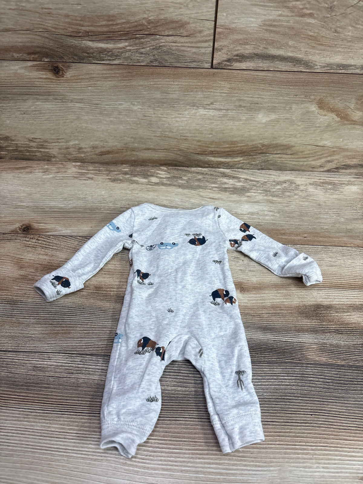 Grey Carter's footless baby sleeper with bison and nature prints on a wood floor