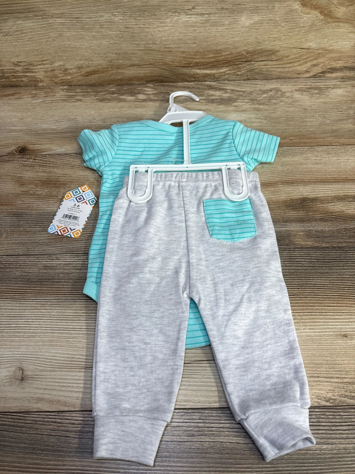 Flat-lay back view of teal striped baby bodysuit and light gray pants with matching teal pocket and size 3-6M tag on wood background