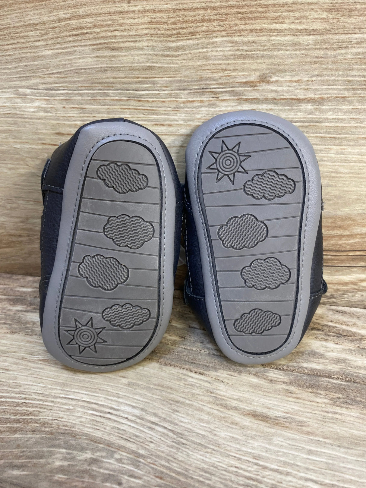 Bottom view of NEW Just One You Harrison fisherman sandals in navy showing gray non-slip soles with cloud and sun pattern on wood