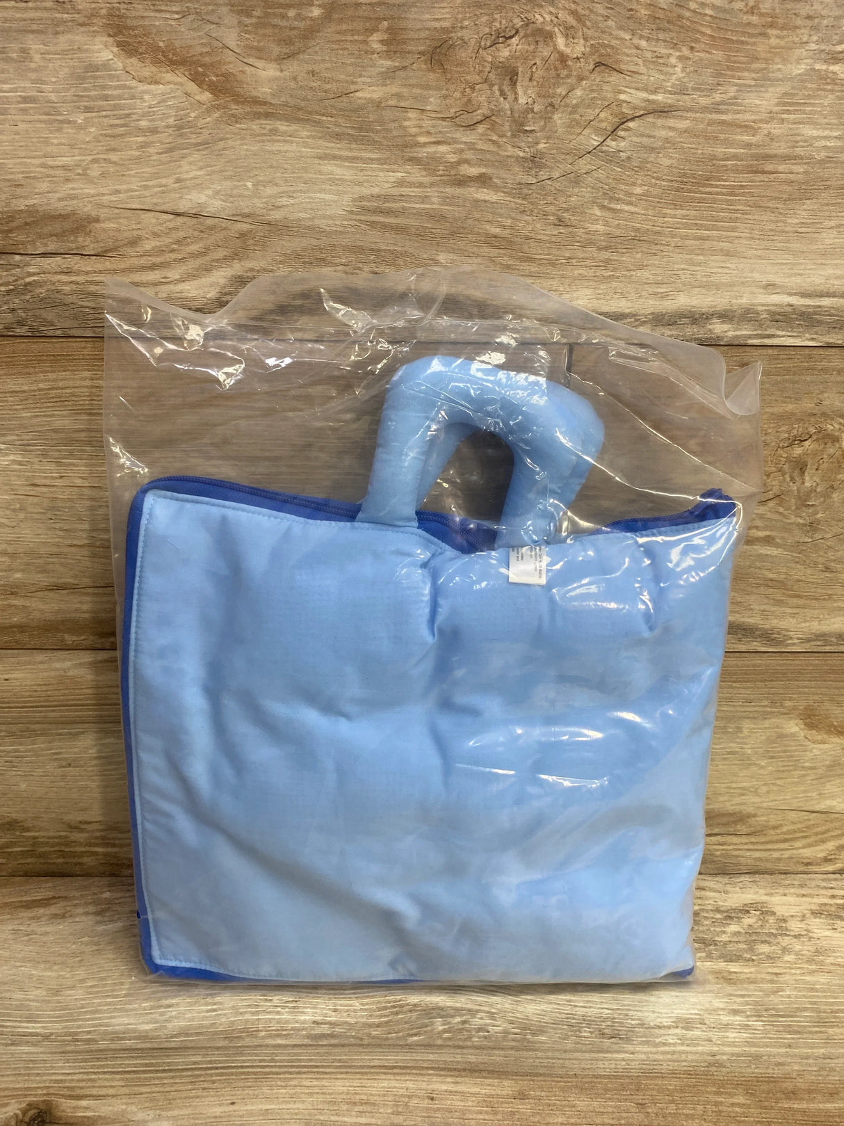 Light blue padded blanket with a built-in handle inside transparent plastic packaging on wooden surface