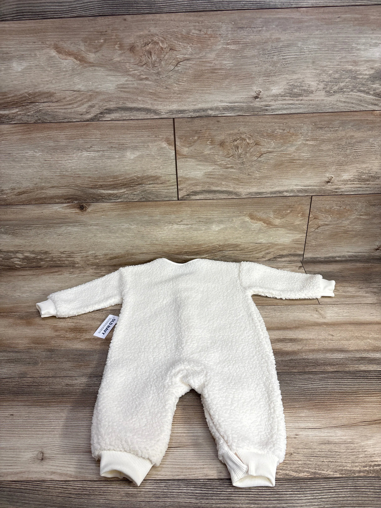 White fleece baby romper with long sleeves on wooden floor background