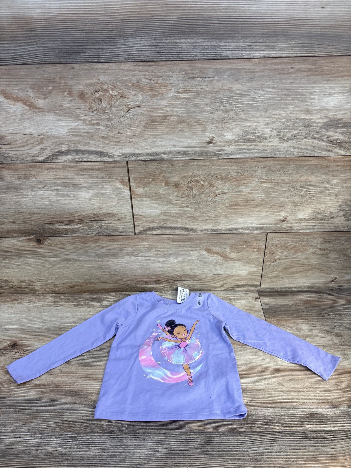 Purple long sleeve toddler shirt with cartoon ballerina and rainbow skirt graphic on wooden floor