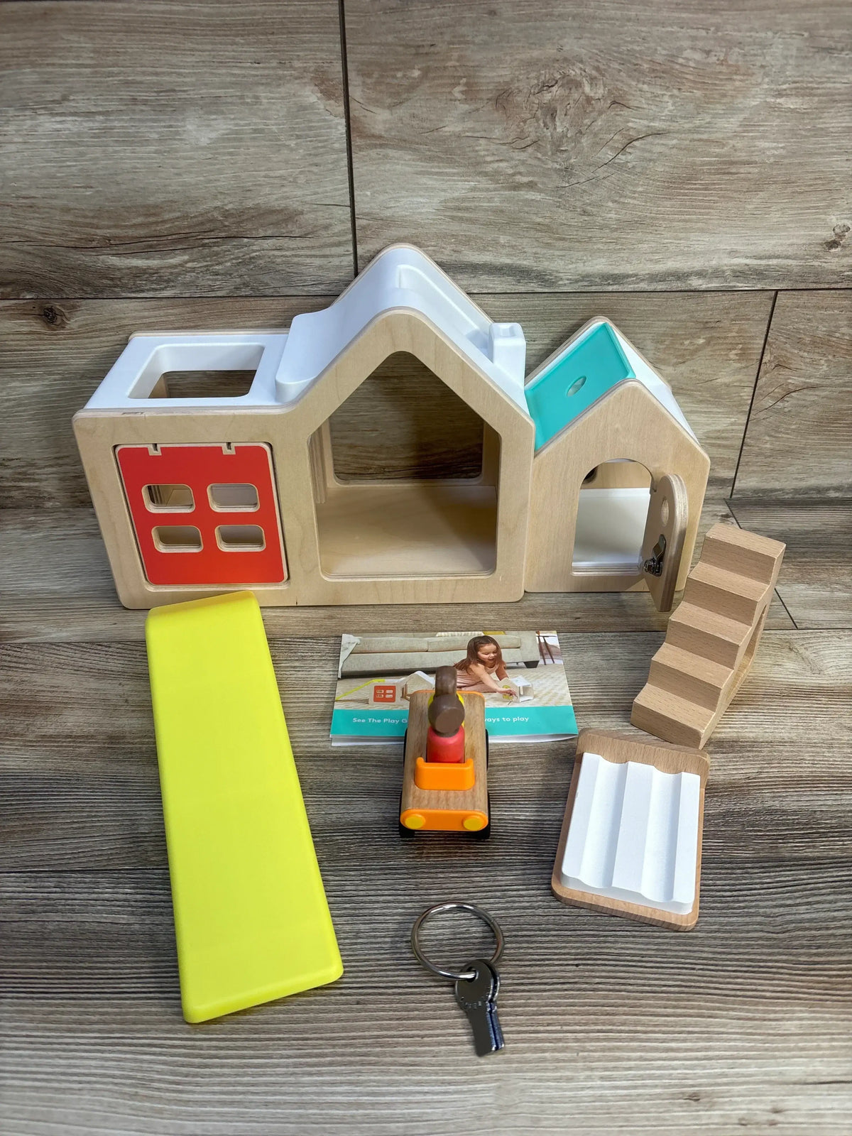 Front view of Lovevery Modular Playhouse with yellow slide, wooden stairs, toy car, working door and key on wood backdrop