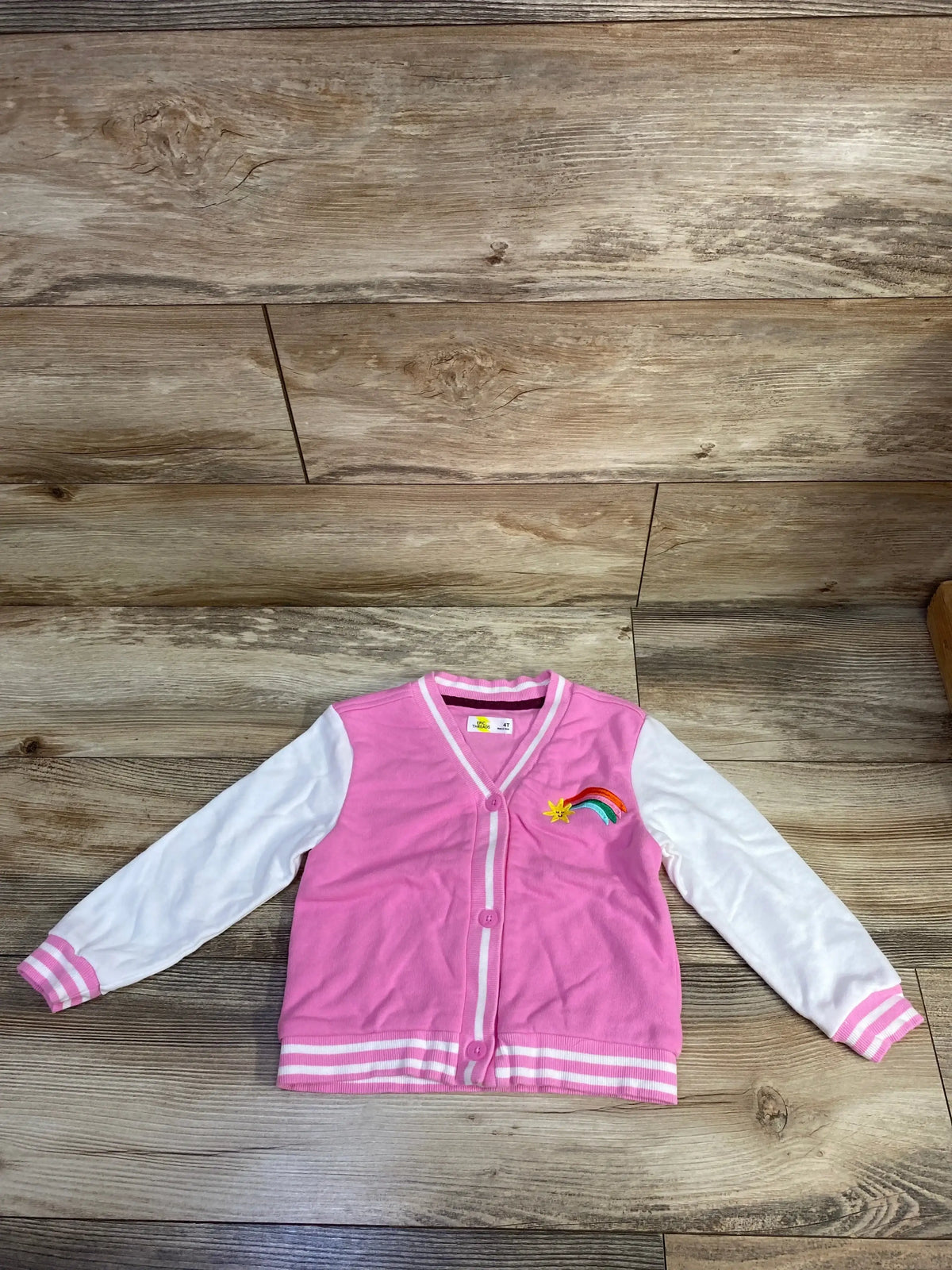 Pink kids' varsity jacket with white sleeves and rainbow patch on wooden floor