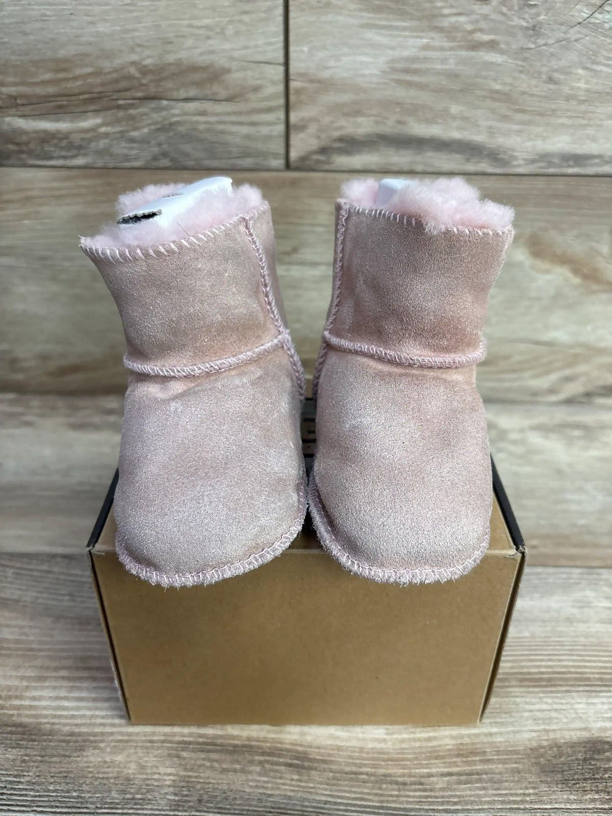 Pair of soft pink baby booties with fluffy lining displayed on a cardboard box on wooden surface