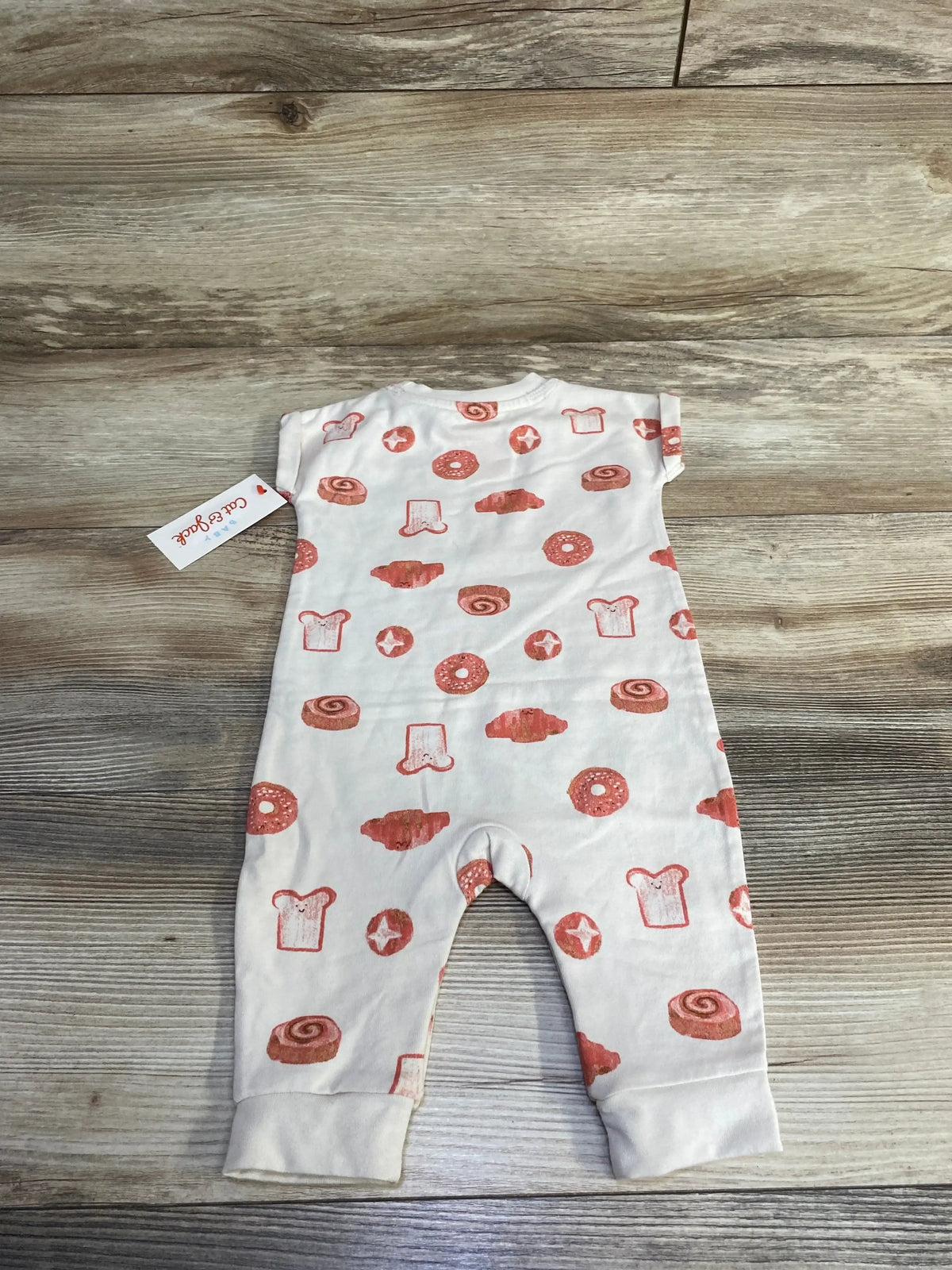 Back view of Cat and Jack newborn coverall showing orange pastry print, short sleeves, cuffed legs on wooden background