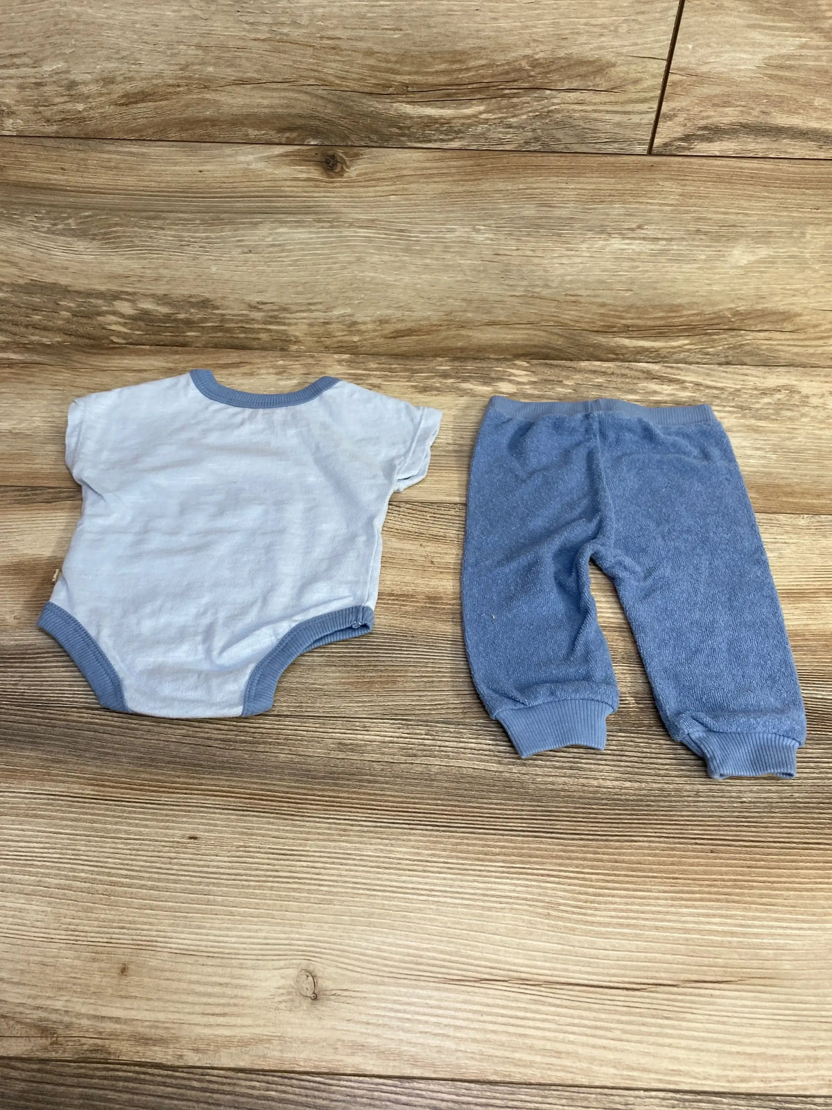 Top down view of Bearpaw blue two piece bodysuit and pants showcasing ribbed trim and cuffed pant ankles on wood floor background