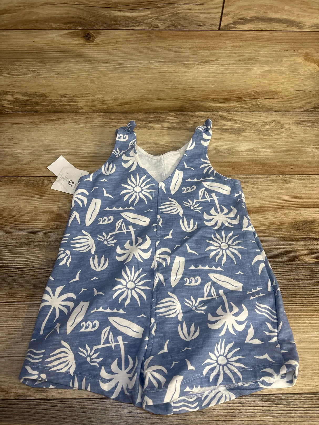 Blue baby romper with white tropical palm tree and surfboard print, laid on wood background.