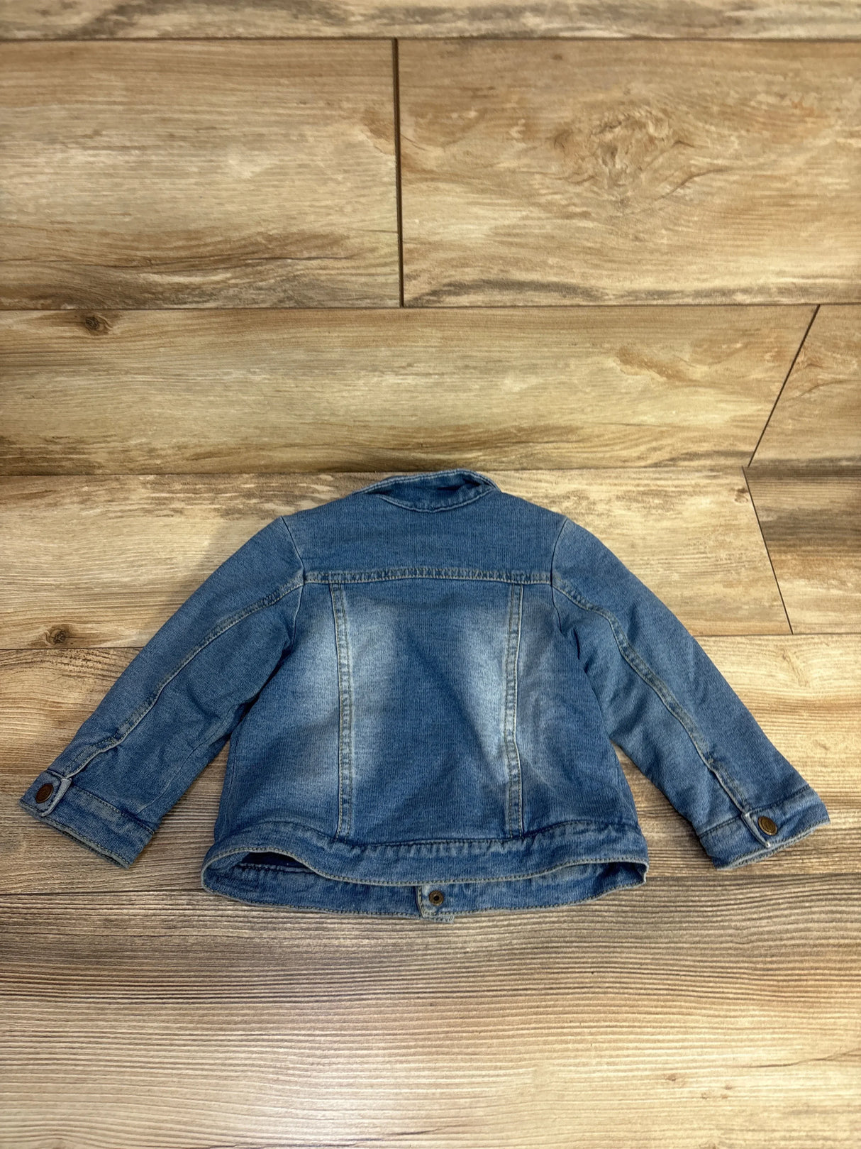 Back view of blue denim jacket with buttoned cuffs on wooden floor