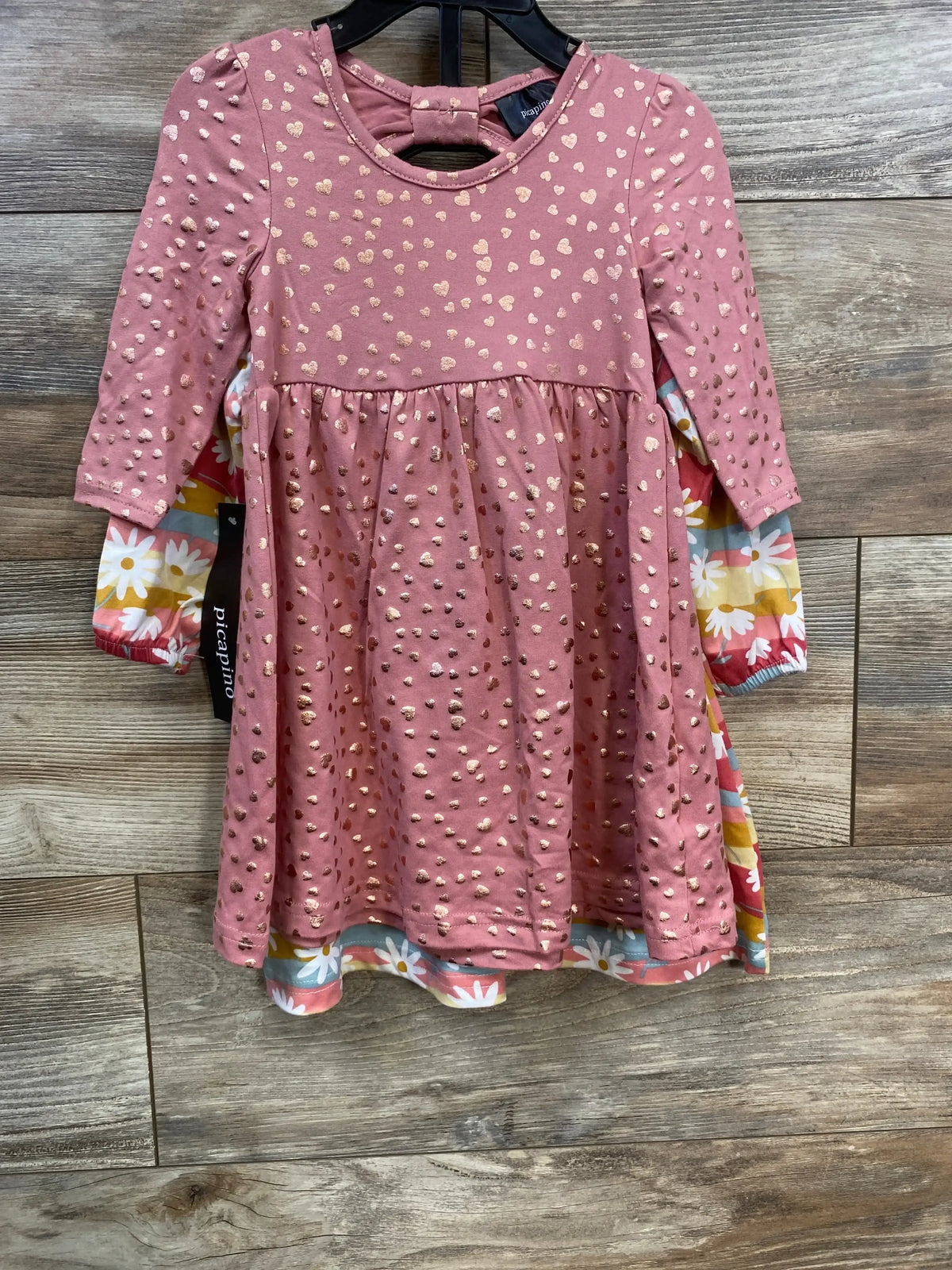 Pink toddler dress with gold heart and dot pattern on wooden floor, layered over floral long sleeve dress