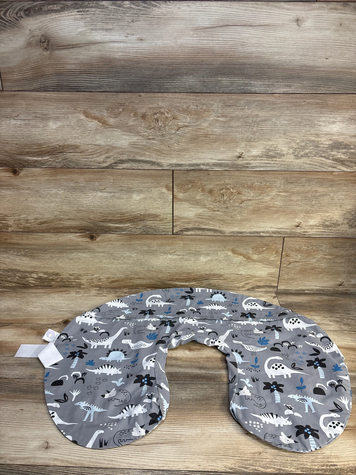 Top-down view of Boppy nursing pillow cover showcasing grey fabric with white, black, and blue dinosaur print on wood plank background