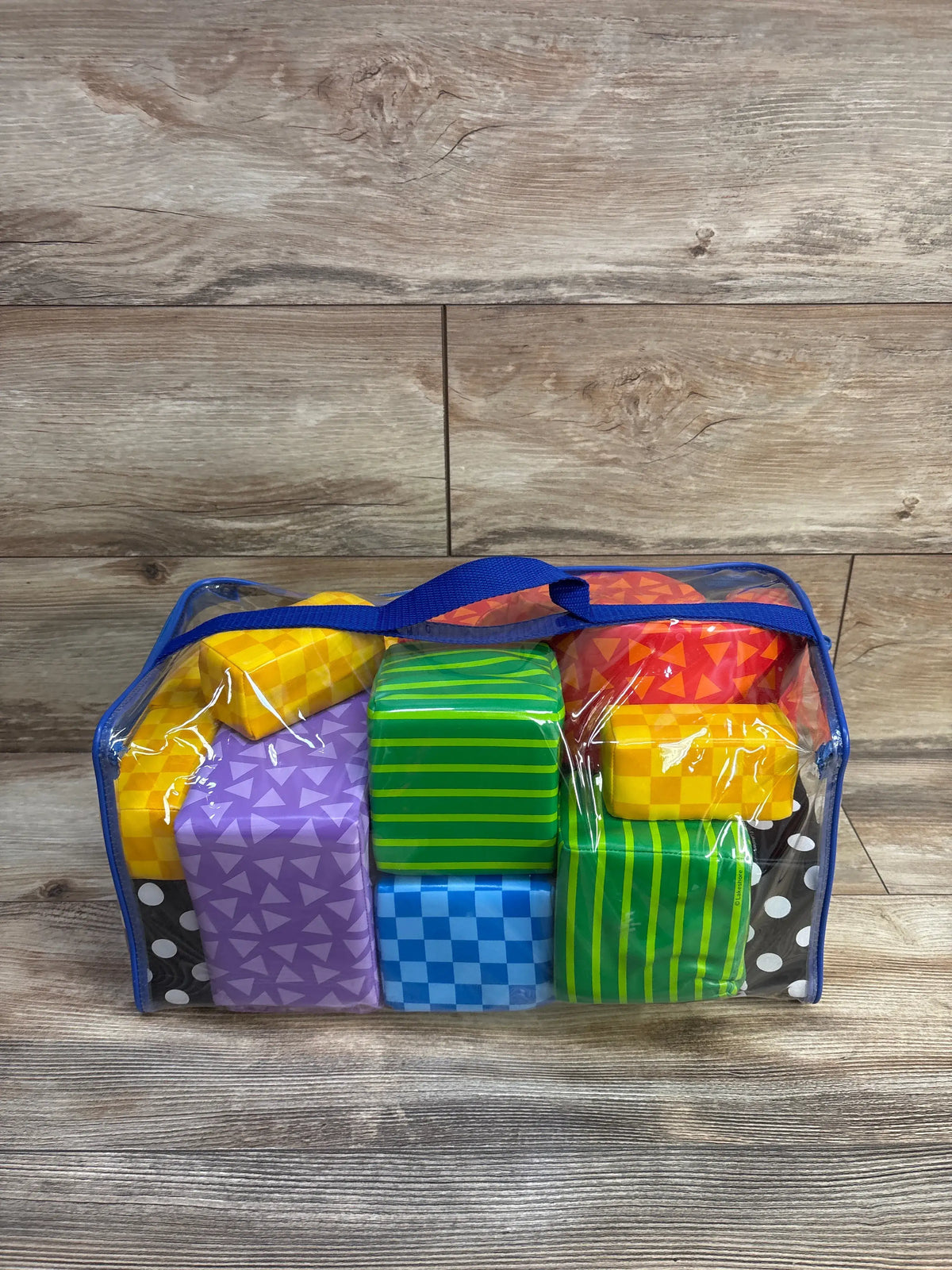 Front view of Lakeshore Soft and Safe building blocks showing colorful patterned foam blocks in clear bag on wood background