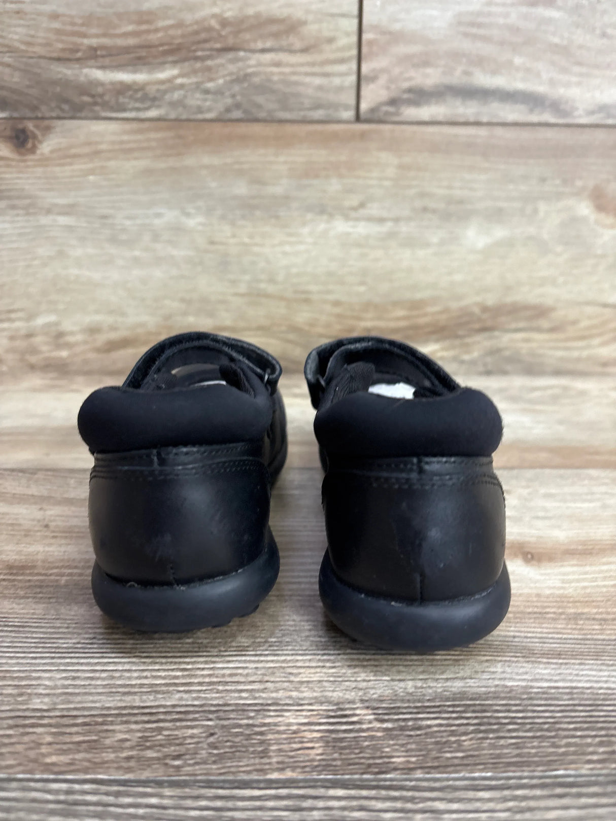 Rear view of black toddler shoes on wood floor background
