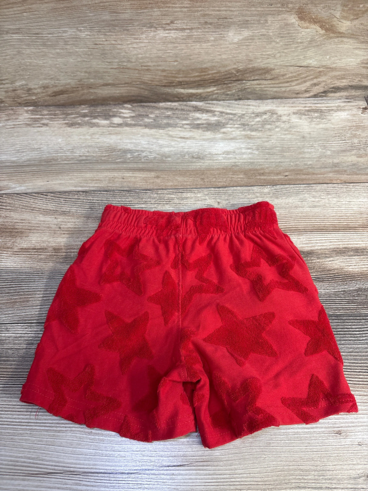 Flat lay of red terry cloth toddler shorts (3T) showing raised star texture and elastic waist on wood background