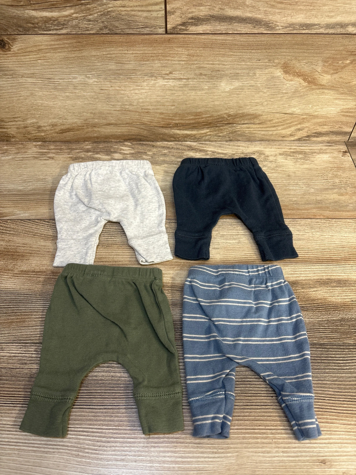 Set of four baby pants in grey, navy, olive green, and blue striped on wood floor