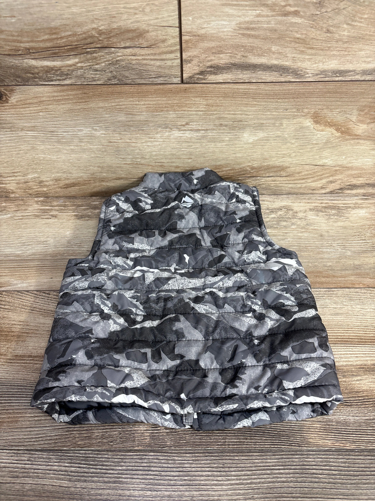 Camo-patterned puffer vest on wooden floor, men's casual insulated outerwear