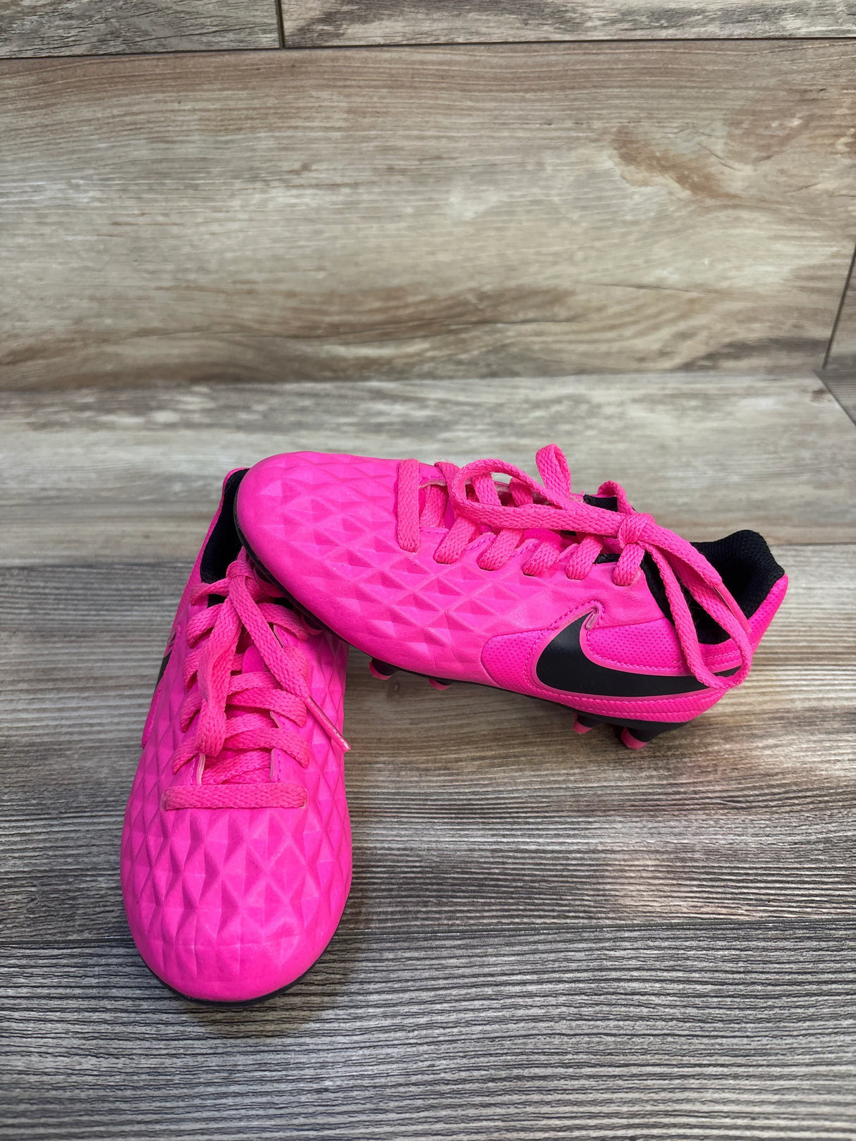 Bright pink kids soccer cleats with black accents on wood floor