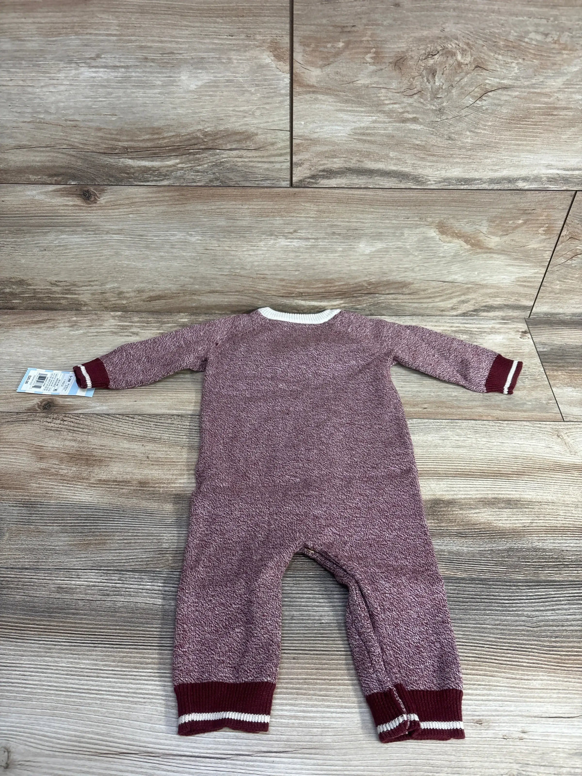 Maroon knit baby jumpsuit with white trim, long sleeves, laid flat on wood floor.