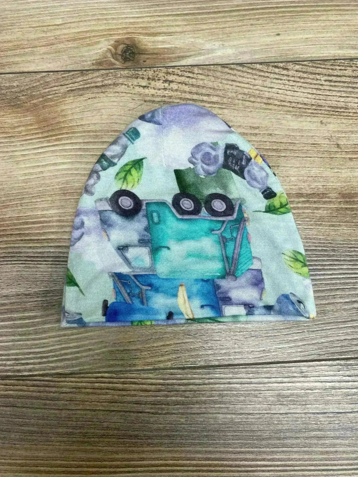 Flat lay of Posh P beanie (0-3 months) showing teal and blue recycling truck print and folded hem on wood background