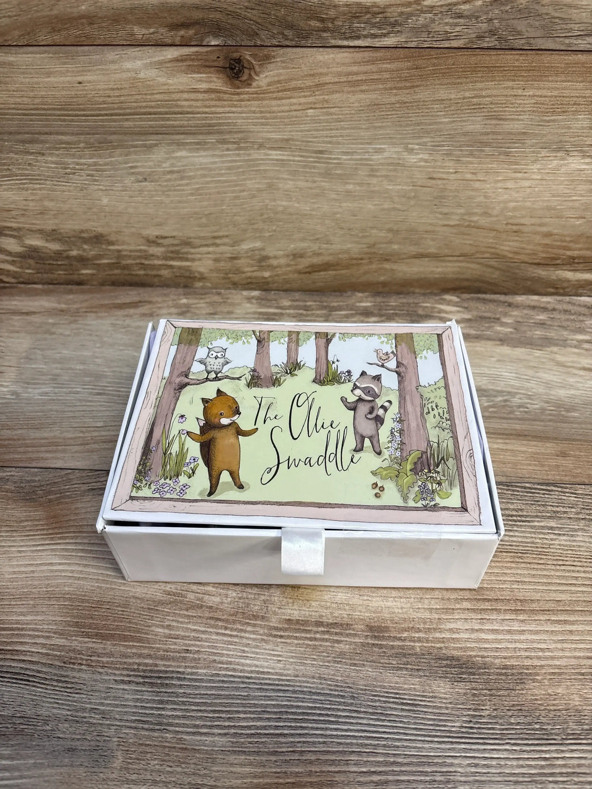 The Ollie Swaddle gift box with woodland animal illustrations on a wood background