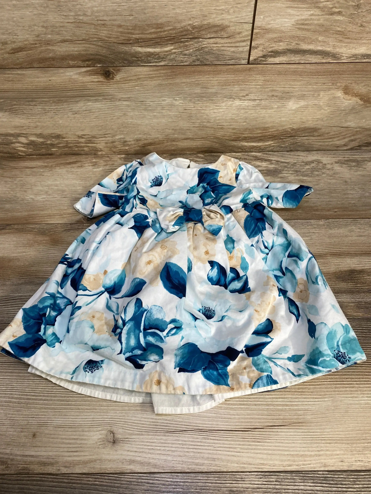 Flat lay of Janie and Jack toddler floral dress showing blue and tan watercolor flowers, waist bow and short sleeves on wood floor