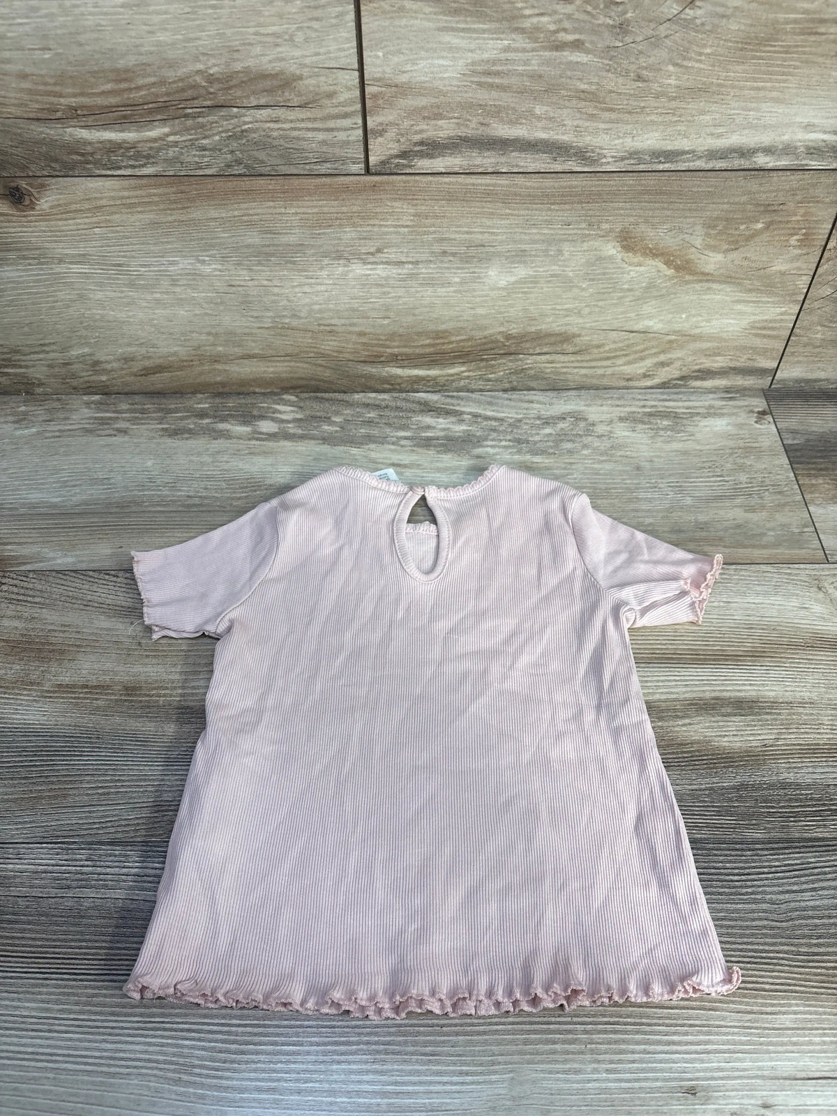 Flat lay of pink H&M ribbed lettuce trim shirt showcasing ribbed fabric and lettuce trim on sleeves and hem on a wood surface
