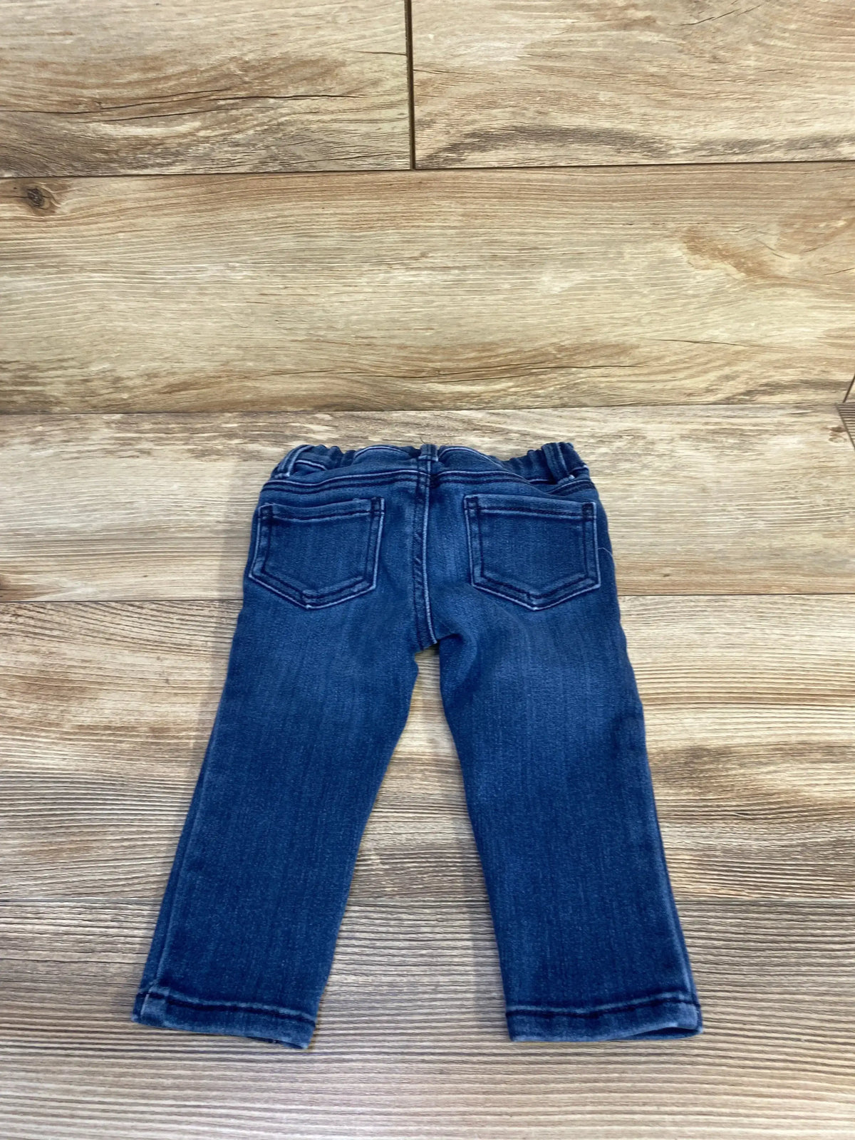 Back view of OshKosh toddler blue triple-button jeans size 12 months showing elastic waistband and back pockets on wood background