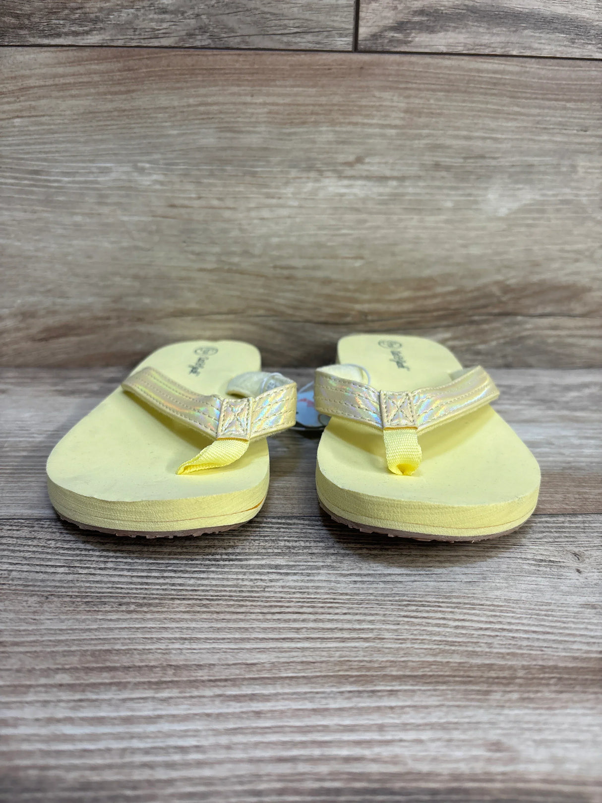 Kids yellow flip flops with iridescent straps on wooden background