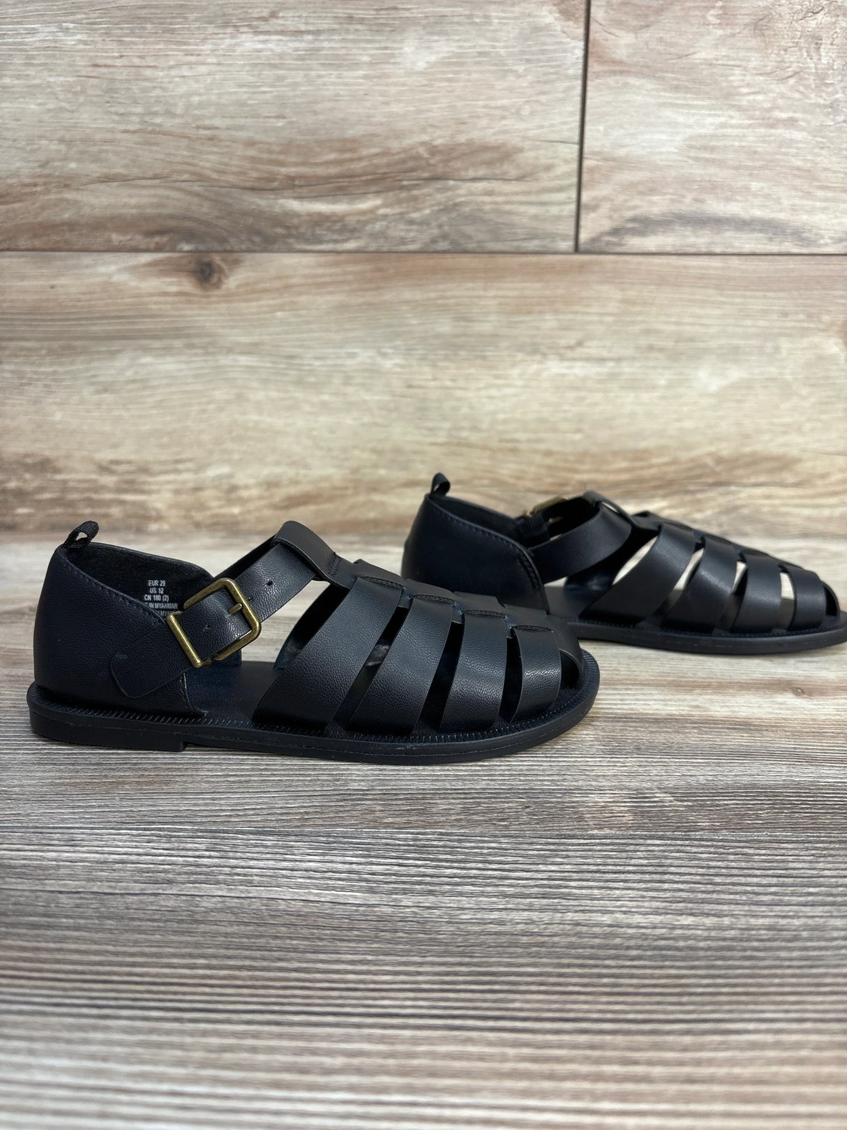 Black leather kids fisherman sandals with buckle, displayed on wood background