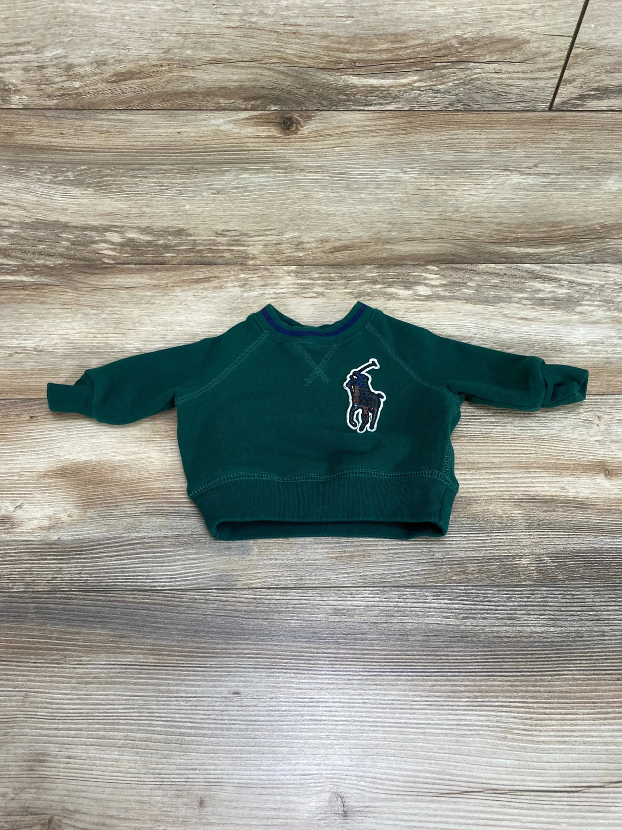 Flat lay of Ralph Lauren green baby fleece sweatshirt (3M) showing embroidered Big Pony logo on chest on wood plank background