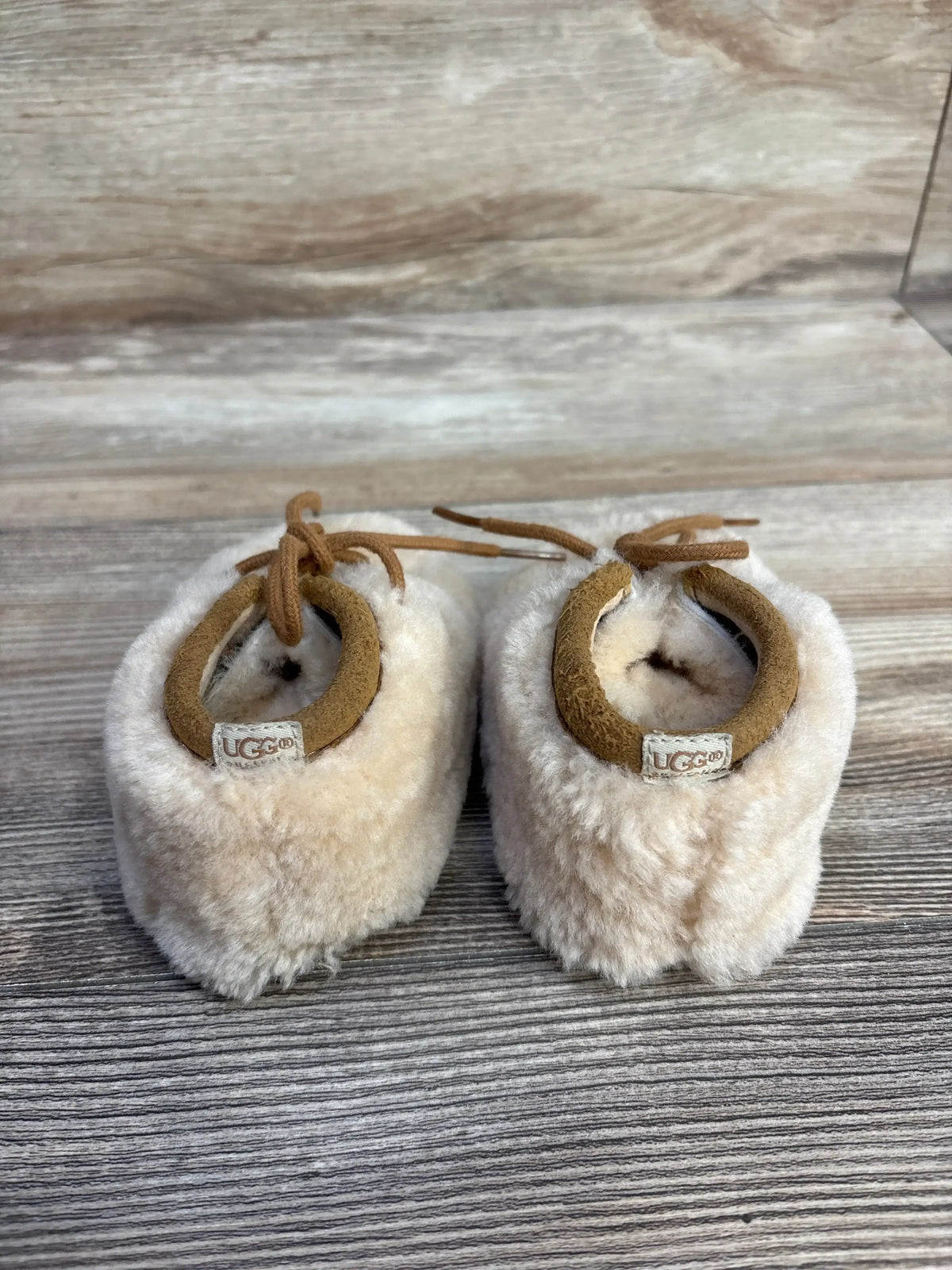 UGG infant shearling boots with tan suede trim on wood background