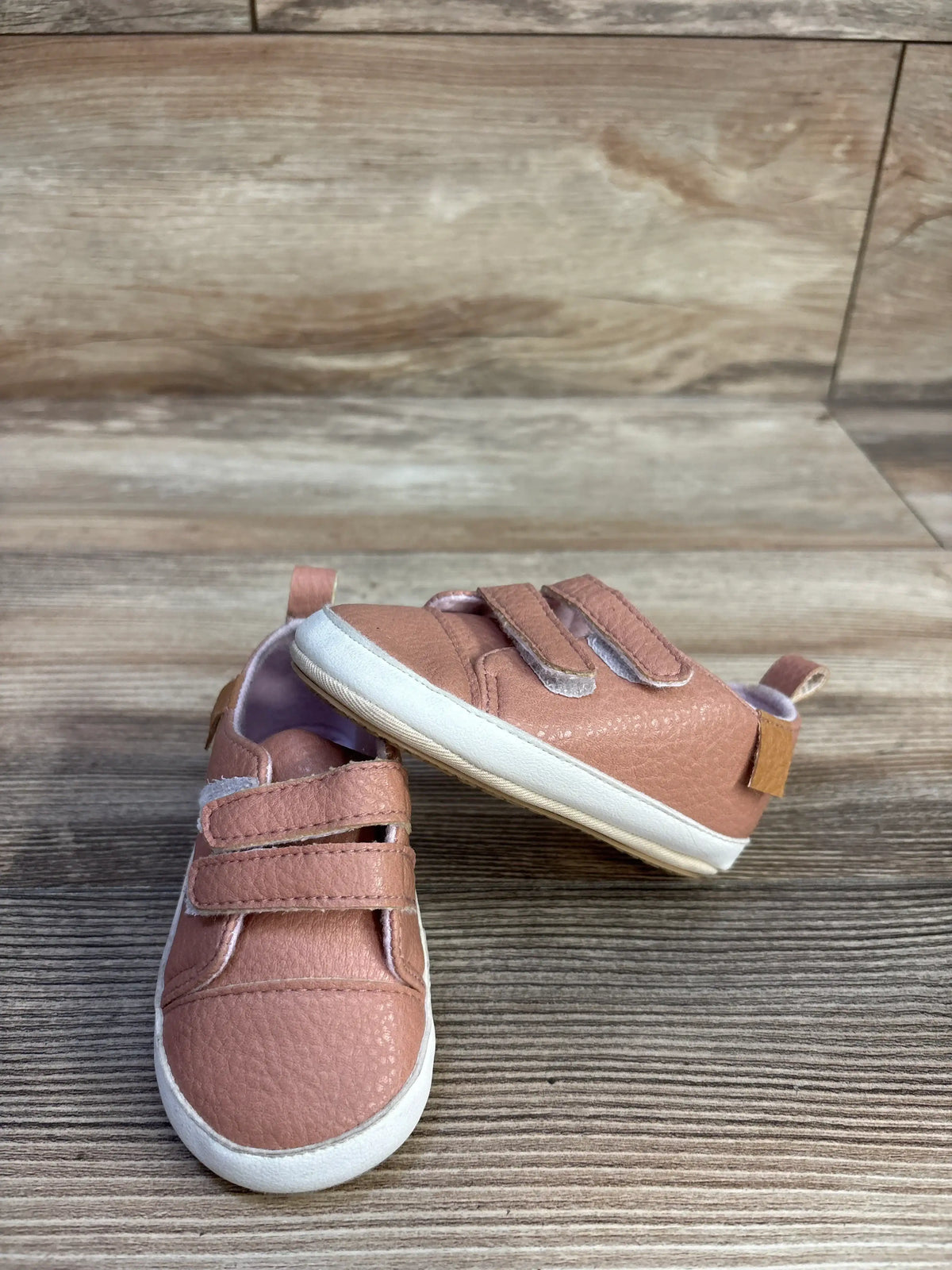 Front and side views of pink Rokment non-slip crib shoes showcasing double straps and pull tabs with a wood-look floor