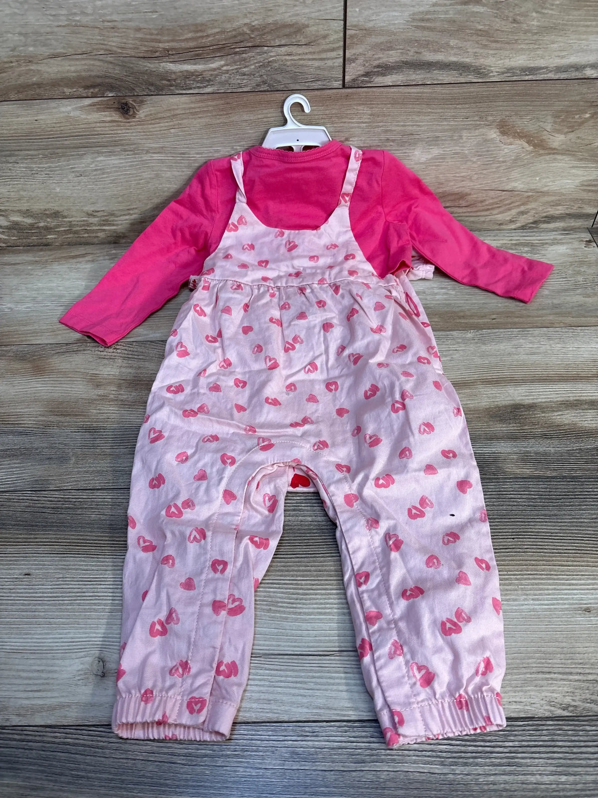 Pink long sleeve toddler shirt with pink heart print overalls on hanger