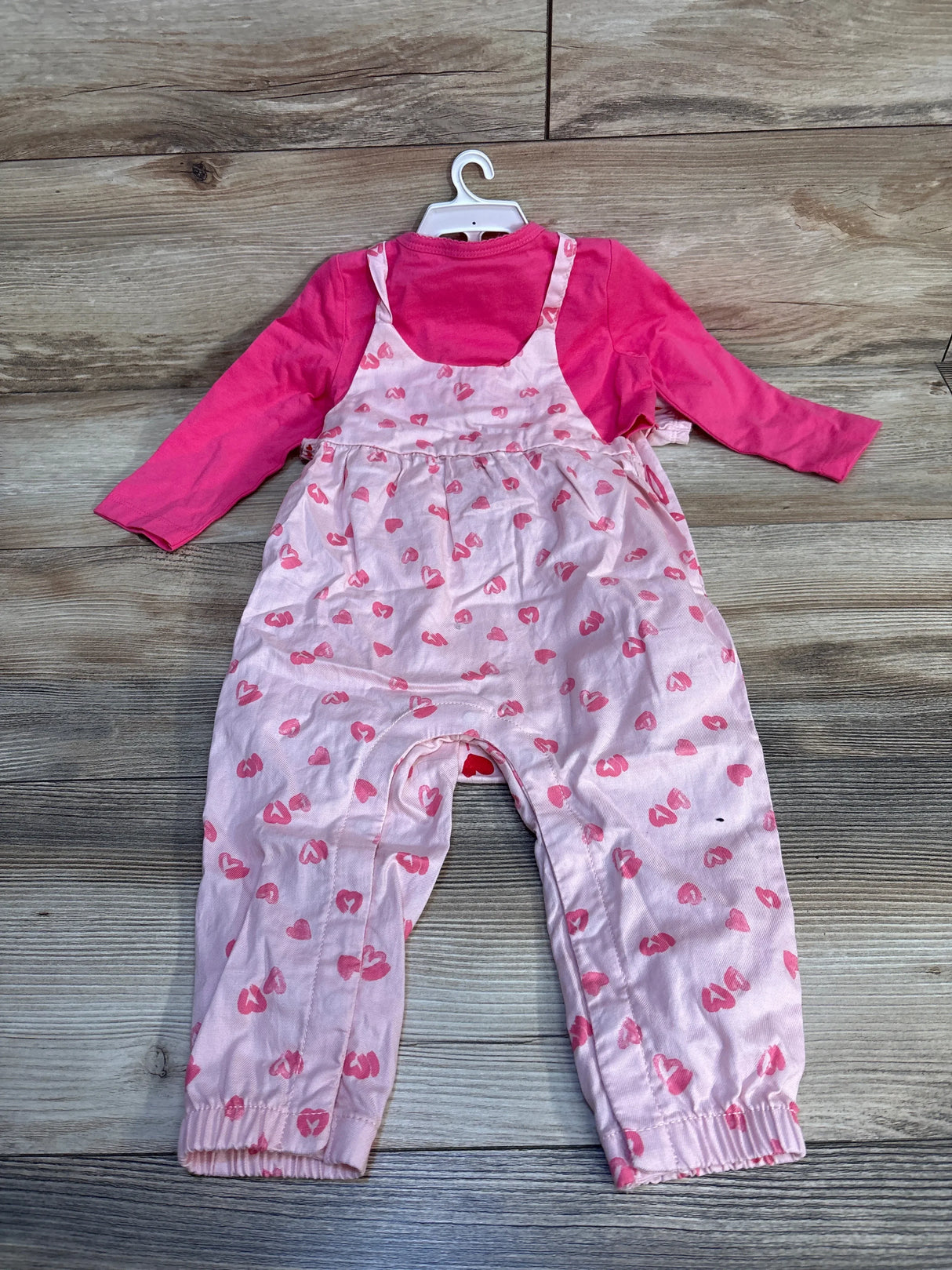Pink long sleeve toddler shirt with pink heart print overalls on hanger