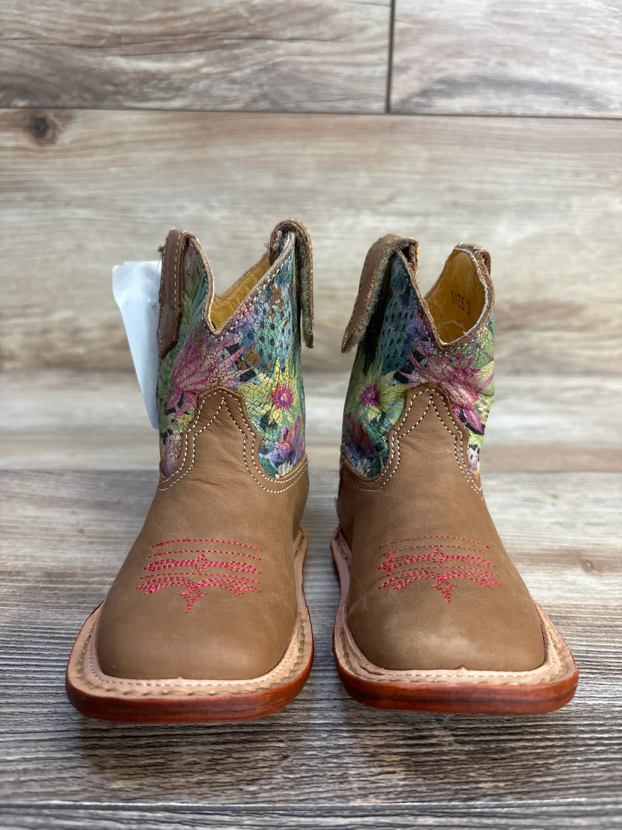 Tan kids cowboy boots with floral embroidered shafts on wooden background