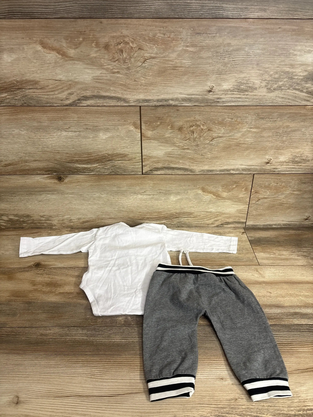 Flat lay of white long-sleeve baby bodysuit and gray jogger pants showing striped elastic waistband and cuffs on light wood background